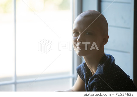 Calm smiling young woman receiving cancer treatment sitting by window 71534622