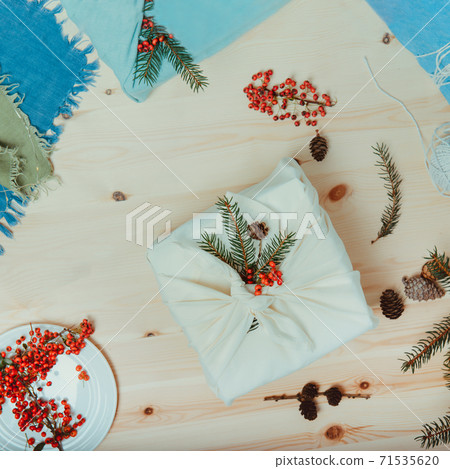 Zero waste christmas concept. Gift box wrapped in white fabric with spruce branch and berries on wooden background. Flatlay. Eco friendly Sustainable lifestile. No plastic. Square card. Copy space. 71535620