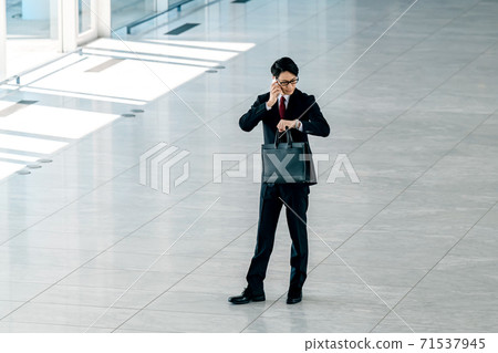 A young businessman in a suit calling on his smartphone in the office 71537945