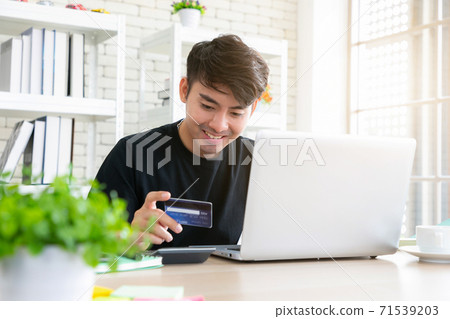 A man paying for online shopping using laptop and credit card. This image is illustrated the online payment concept via smartphone. A man paying for online shopping using laptop and credit card. This image is illustrated the online payment concept via smartphone. 71539203