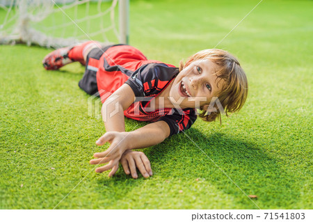 Little cute kid boy in red football uniform playing soccer, football on field, outdoors. Active child making sports with kids or father, Smiling happy boy having fun in summer 71541803