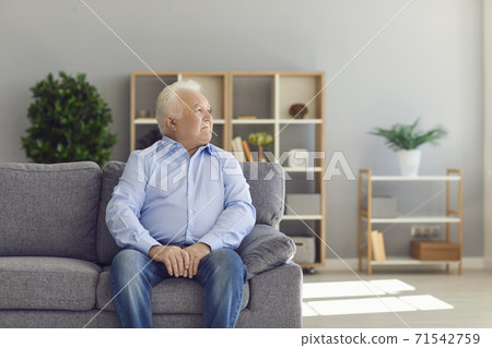 Senior man sitting on sofa in living room thinking about life and recollecting memories of the past 71542759