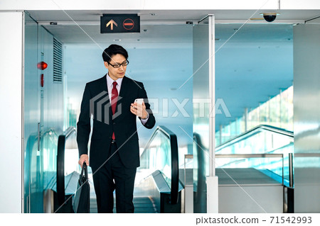 一個通勤的商人,看著他的智能手機下自動扶梯 一個通勤的商人,看著他的智能手機下自動扶梯 71542993