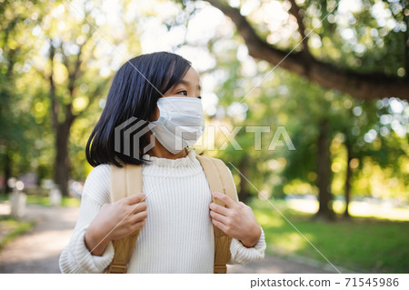 Portrait of small Japanese girl with backpack walking outdoors in town, coronavirus concept. 71545986