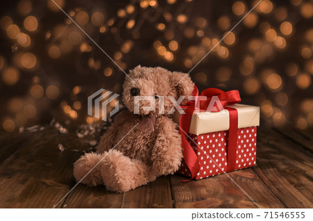 Teddy bear and gift box with bow. Christmas gift and light from garlands with gold bokeh on the Teddy bear and gift box with bow. Christmas gift and light from garlands with gold bokeh on the 71546555