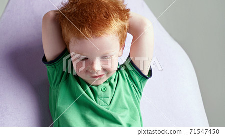 Cute red haired freckled little boy in green t-shirt waiting for doctor in medical office Cute red haired freckled little boy in green t-shirt waiting for doctor in medical office 71547450