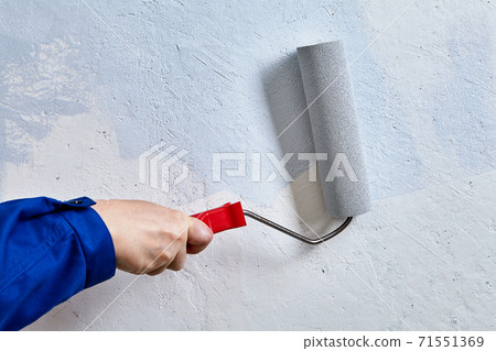 Handyman paints wall by paint and painting roller during renovation. 71551369