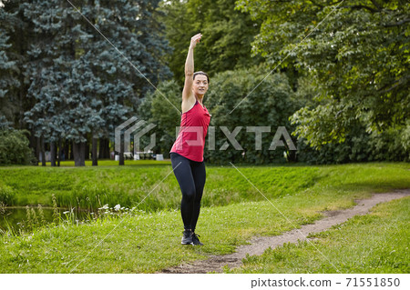 Active white woman trains in city garden for healthy near pond. 71551850