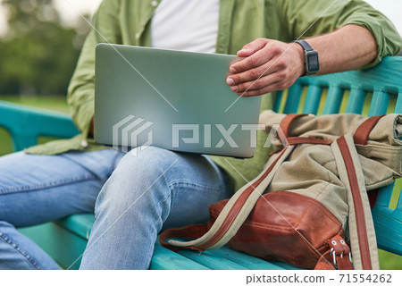 Cropped shot of young man using laptop while working, sitting on the bench outdoors  71554262