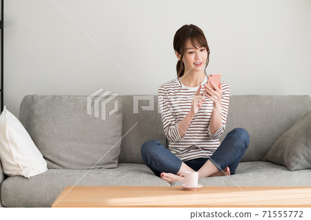 A woman operating a smartphone on the sofa 71555772