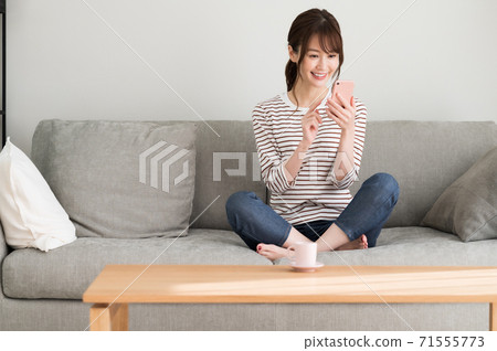 A woman operating a smartphone on the sofa 71555773