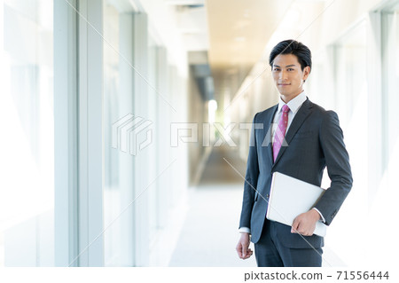 Portrait of a young man standing with a computer in the office corridor 71556444