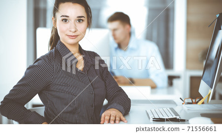 Business woman using computer at workplace in modern office. Brunette secretary or female lawyer looking at the camera and happy smiling. Working for pleasure and success Business woman using computer at workplace in modern office. Brunette secretary or female lawyer looking at the camera and happy smiling. Working for pleasure and success 71556661