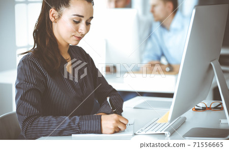 Business woman using computer at workplace in modern office. Brunette secretary or female lawyer looking at the camera and happy smiling. Working for pleasure and success Business woman using computer at workplace in modern office. Brunette secretary or female lawyer looking at the camera and happy smiling. Working for pleasure and success 71556665