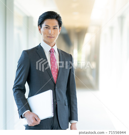 Portrait of a young man standing with a computer in the office corridor Square 71556944