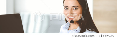 Brunette female customer service representative in a headset is consulting clients online. Call center and business people concept 71556989