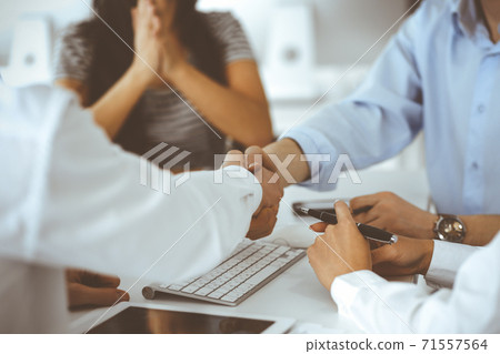 Two businessmen are shaking hands in office while sitting at the desk, close-up. Colleagues applauding of success meeting end. Business people concept 71557564