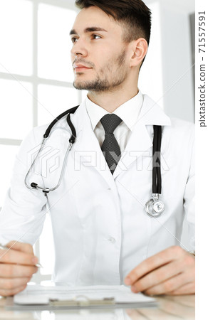 Doctor man filling up medication history records form while sitting at the glass desk in clinic. Medicine and healthcare concept 71557591