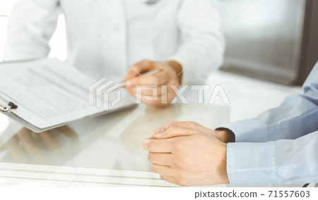 Unknown male doctor and woman-patient discussing current health examination while sitting in clinic and using clipboard. Good medical service in hospital. Medicine concept 71557603