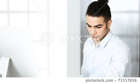 Businessman is working with computer in modern office. Headshot of arab male entrepreneur at workplace. Business concept Businessman is working with computer in modern office. Headshot of arab male entrepreneur at workplace. Business concept 71557656