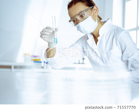 Female laboratory assistant analyzing test tube with blue liquid. Medicine, health care and researching concept Female laboratory assistant analyzing test tube with blue liquid. Medicine, health care and researching concept 71557770