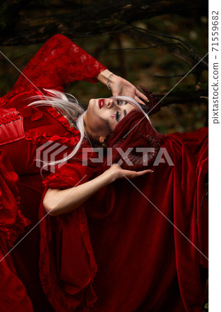 Maleficent Woman in Red Clothing and Horns in dark Forest. Posing in magik forest Maleficent Woman in Red Clothing and Horns in dark Forest. Posing in magik forest 71559682