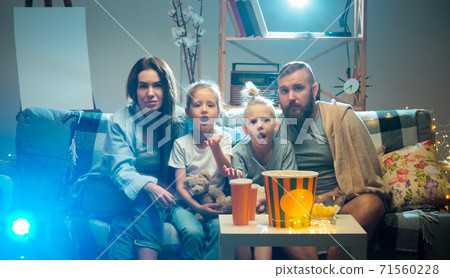 Happy family watching projector, TV, movies with popcorn in the evening at home. Mother, father and kids spending time together. 71560228