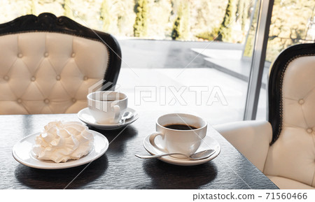 Two cups of black coffee with meringue on a textured dark wood table in a cafe with classical interior. Two cups of black coffee with meringue on a textured dark wood table in a cafe with classical interior. 71560466