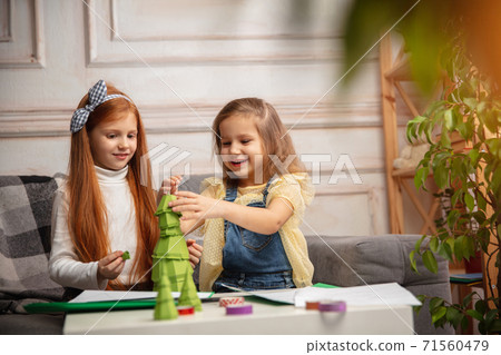 Two little children, girls together in creativity of the house. Happy kids make handmade toys for games or New Year celebration Two little children, girls together in creativity of the house. Happy kids make handmade toys for games or New Year celebration 71560479