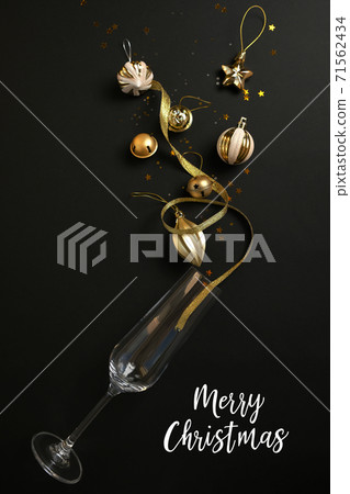 Wine glasses with golden confetti and stars with the inscription Merry Christmas on black background. Holiday and celebration concept. Wine glasses with golden confetti and stars with the inscription Merry Christmas on black background. Holiday and celebration concept. 71562434
