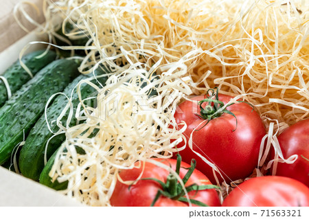 Wooden and cardboard crate box with fresh ripe tasty red tomatoes and green cucumbers with wood shavings filler delivered by unmanned shipping postage mail service. Farmers selected bio vegetables 71563321