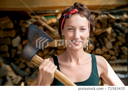 Young adult beautiful happy attractive caucasian brunette woman portrait have fun enjoy holding old rusty axe chopping firewood at wood store on backyard. Feminine women equality empowerment concept Young adult beautiful happy attractive caucasian brunette woman portrait have fun enjoy holding old rusty axe chopping firewood at wood store on backyard. Feminine women equality empowerment concept 71563435