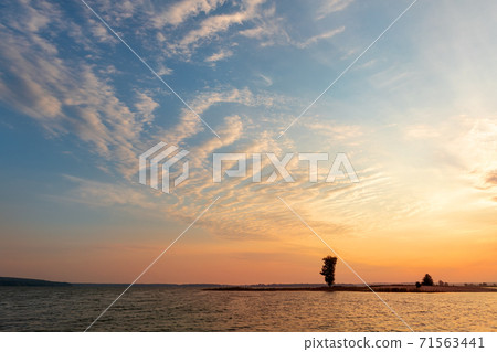 Dramatic colorful orange to blue sunset or sunrise sky landscape with lake or river bank and tree silhouette. Natural beautiful cloudscape dawn wallpaper.Ripple water reflection twilight panorama 71563441
