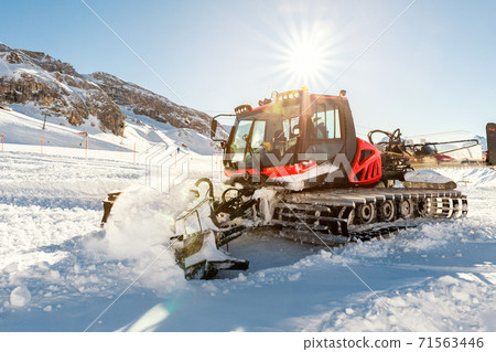 Red modern snowcat ratrack with snowplow snow grooming machine preparing ski slope piste hill at alpine skiing winter resort Ischgl in Austria. Heavy machinery mountain equipment track vehicle 71563446