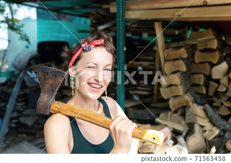 Young adult beautiful happy attractive caucasian brunette woman portrait have fun enjoy holding old rusty axe chopping firewood at wood store on backyard. Female person vintage retro pinup style 71563458