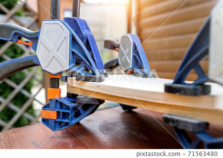 Joining wooden handmade box with clamps joiners after glueing. Different chisels, drills and pencils at craftsman workshop. DIY instruments on wood workbench. Workplace organization arrangement 71563480
