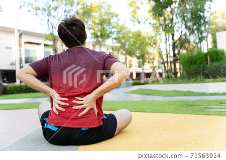 Male athlete suffering from back pain and injury. Hands grab back or waist after running in the park. Male athlete suffering from back pain and injury. Hands grab back or waist after running in the park. 71563914