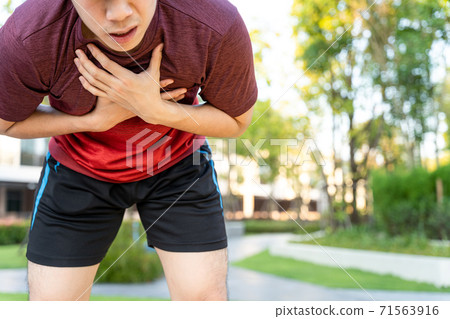 Exhausted male runner athlete suffering painful angina pectoris or asthma breathing problems while running in the park. Exhausted male runner athlete suffering painful angina pectoris or asthma breathing problems while running in the park. 71563916
