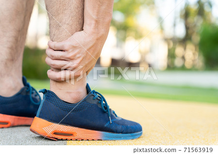Male runner athlete leg injury and pain. Hands grab painful leg while running in the park. Male runner athlete leg injury and pain. Hands grab painful leg while running in the park. 71563919