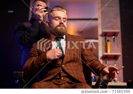hairstylist cutting hair to business man smoking in salon 71565399