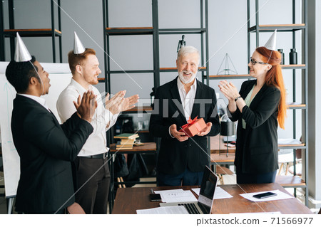 Happy business team of multiethnic businessmen giving present to smiling mature adult male leader. Happy business team of multiethnic businessmen giving present to smiling mature adult male leader. 71566977