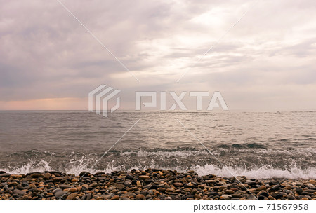 Rain clouds over the sea at sunset. Pebbles on the beach close-up, clouds colored the shades of pink and little waves on the water. Rain clouds over the sea at sunset. Pebbles on the beach close-up, clouds colored the shades of pink and little waves on the water. 71567958
