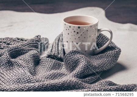 Silvery grey knitted fabric along a cup of tea on milky white fur background. Silvery grey knitted fabric along a cup of tea on milky white fur background. 71568295