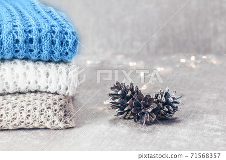 Stylish knitted pastel colored sweaters and one in trendy blue color folded in stack with pine cones and christmas lights on velvety fabric background. Winter and spring season knitwear clothing. Stylish knitted pastel colored sweaters and one in trendy blue color folded in stack with pine cones and christmas lights on velvety fabric background. Winter and spring season knitwear clothing. 71568357