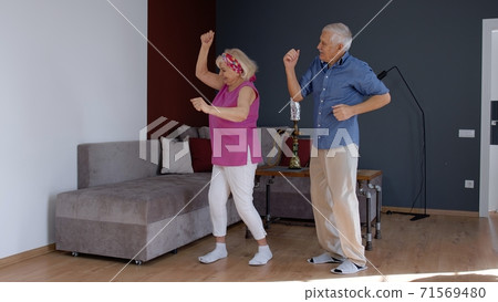Happy old senior couple dancing having fun celebrating retirement anniversary in living room at home Happy old senior couple dancing having fun celebrating retirement anniversary in living room at home 71569480