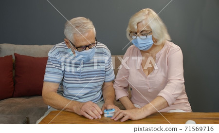 Senior couple grandfather and grandmother monitoring oxygen saturation with digital pulse oximeter 71569716