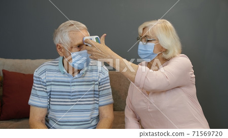 Senior couple measures temperature with contactless digital thermometer during coronavirus lockdown Senior couple measures temperature with contactless digital thermometer during coronavirus lockdown 71569720