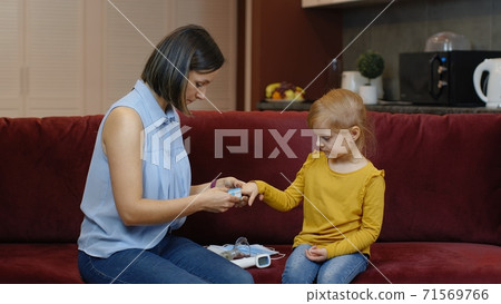 Mother measuring, monitoring oxygen saturation with digital pulse oximeter of her daughter at home Mother measuring, monitoring oxygen saturation with digital pulse oximeter of her daughter at home 71569766