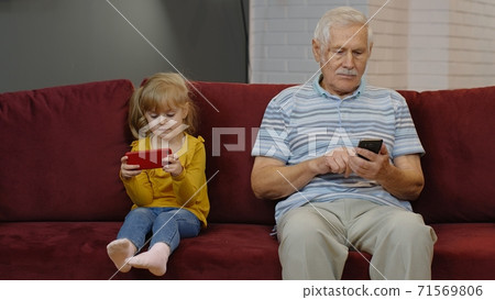 Senior grandfather with child girl granddaughter using digital mobile phone, playing games at home 71569806