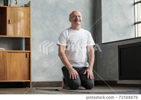 Senior man practicing yoga at home sitting in Vajrasana pose. Senior man practicing yoga at home sitting in Vajrasana pose. 71569879